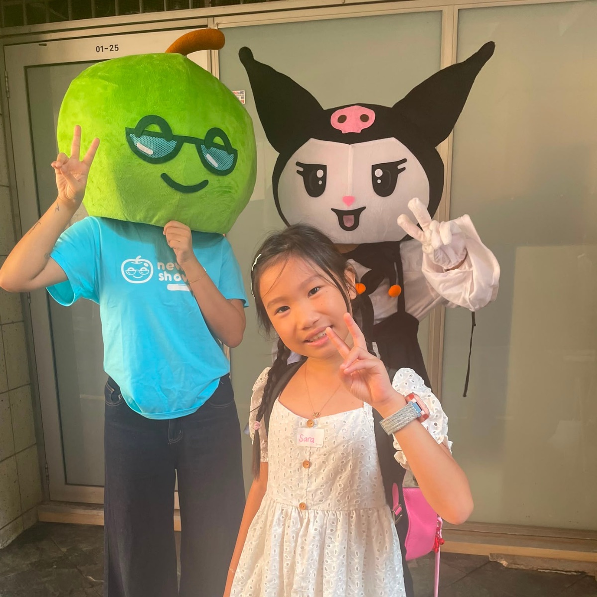 Two Newtonshow mascots posing with a smiling camper outside a Newtonshow campus
