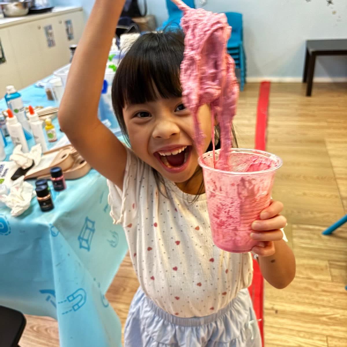 Delighted girl holding up a long strand of bright pink slime she made at a Newtonshow camp
