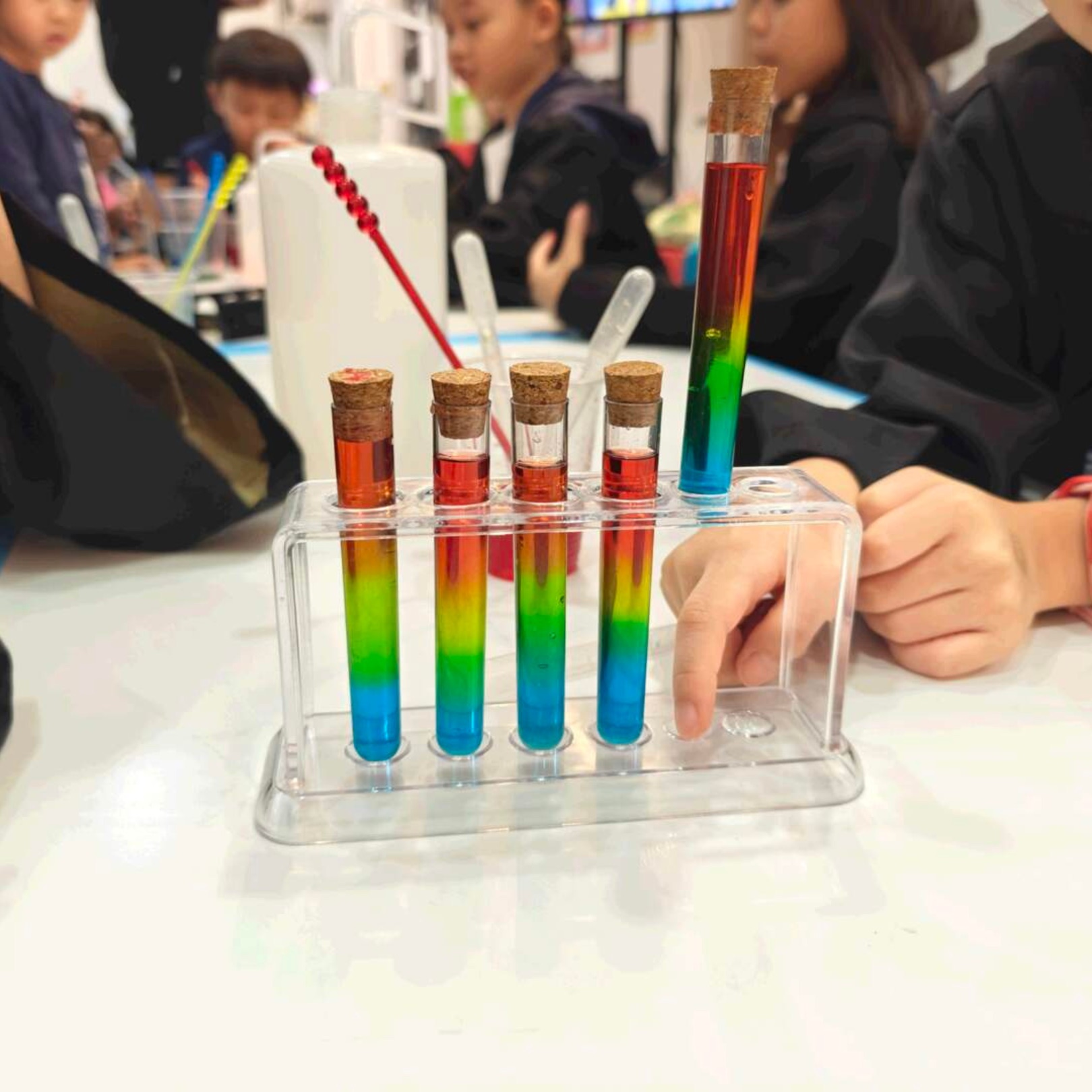 Rack of rainbow-layered potion test tubes made by guests at a Newtonshow party